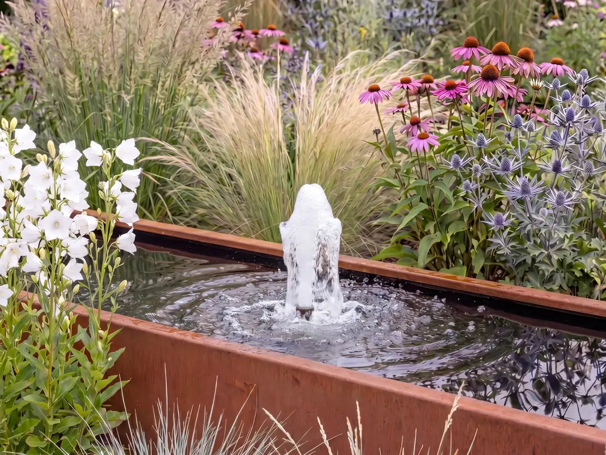 Teichbecken aus Cortenstahl mit Schaumsprudler als Gartenbrunnen einem Garten mit vielen Pflanzen