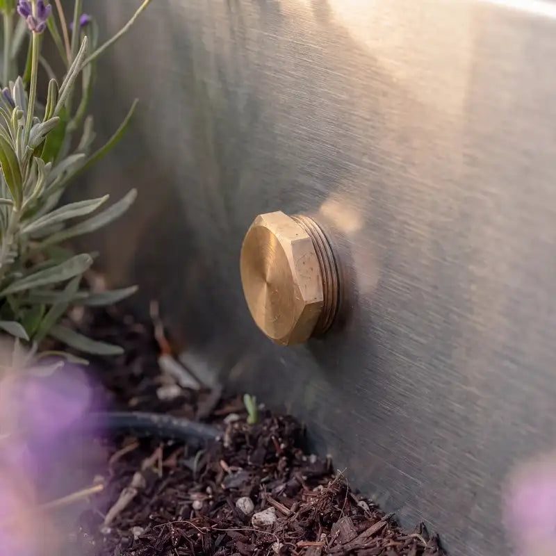 Detailbild von einem Ablassventil aus Messing eines Edelstahl-Wasserbeckens im Garten.