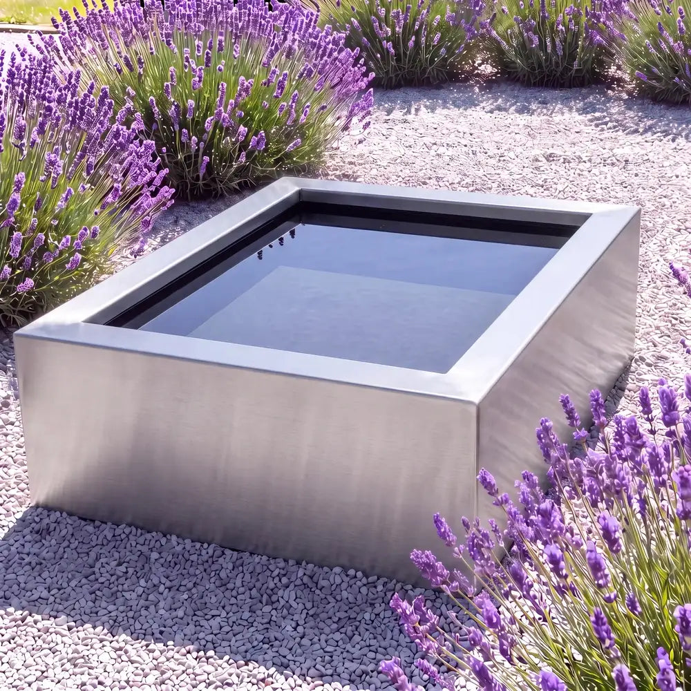 Edelstahl-Hochteich in quadratischer Form mit spiegelnder Wasseroberfläche in einem minimalen Garten.