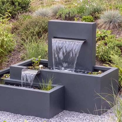 Aluminium-Kaskadenbrunnen mit versetzten Metall-Wasserbecken auf einer Kiesfläche vor einem begrünten Abhang.