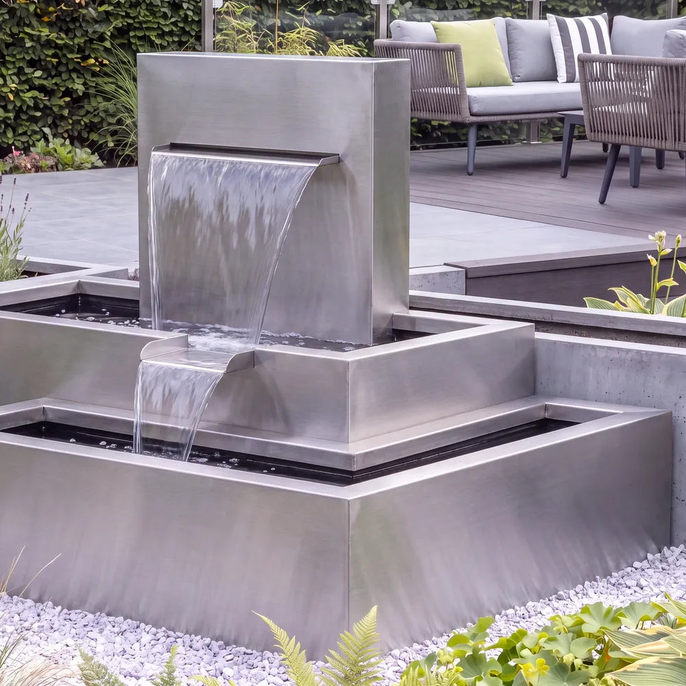 Modernes Wasserspiel mit einem stufigen Kaskadenbrunnen aus Edelstahl in einem modernen Garten.