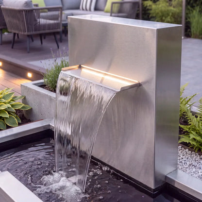 Kaskadenbrunnen aus Edelstahl mit Beleuchtung der Edelstahl-Wasserschütte am Abend vor einer modernen Terrasse.