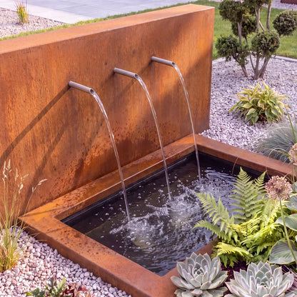 Freistehende Teichwand aus Cortenstahl mit drei Wassereinläufen vor einem versenkten Teichbecken aus GFK und Becken-Umrandung im Garten.