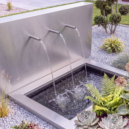 Freistehende Teichwand aus Edelstahl mit drei Wassereinläufen vor einem versenkten Teichbecken aus GFK und Becken-Umrandung im Garten.