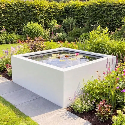 Hohes quadratisches Aluminium-Wasserbecken mit Seerosen im Wasser in einem grünen Blumenbeet im Garten.