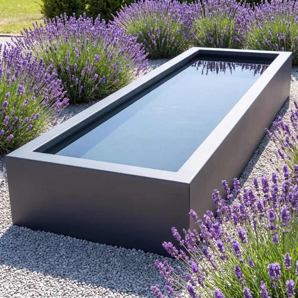 Rechteckiger Aluminium-Teich mit spiegelglatter Wasseroberfläche auf einer Fläche aus Kies und Lavendel-Pflanzen in einem modernen Garten.