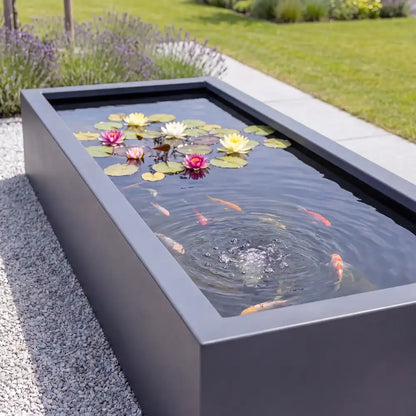 Rechteckiges Wasserbecken aus Aluminium mit Seerosen und Fisch auf einer Kiesfläche in einem modernen Garten.