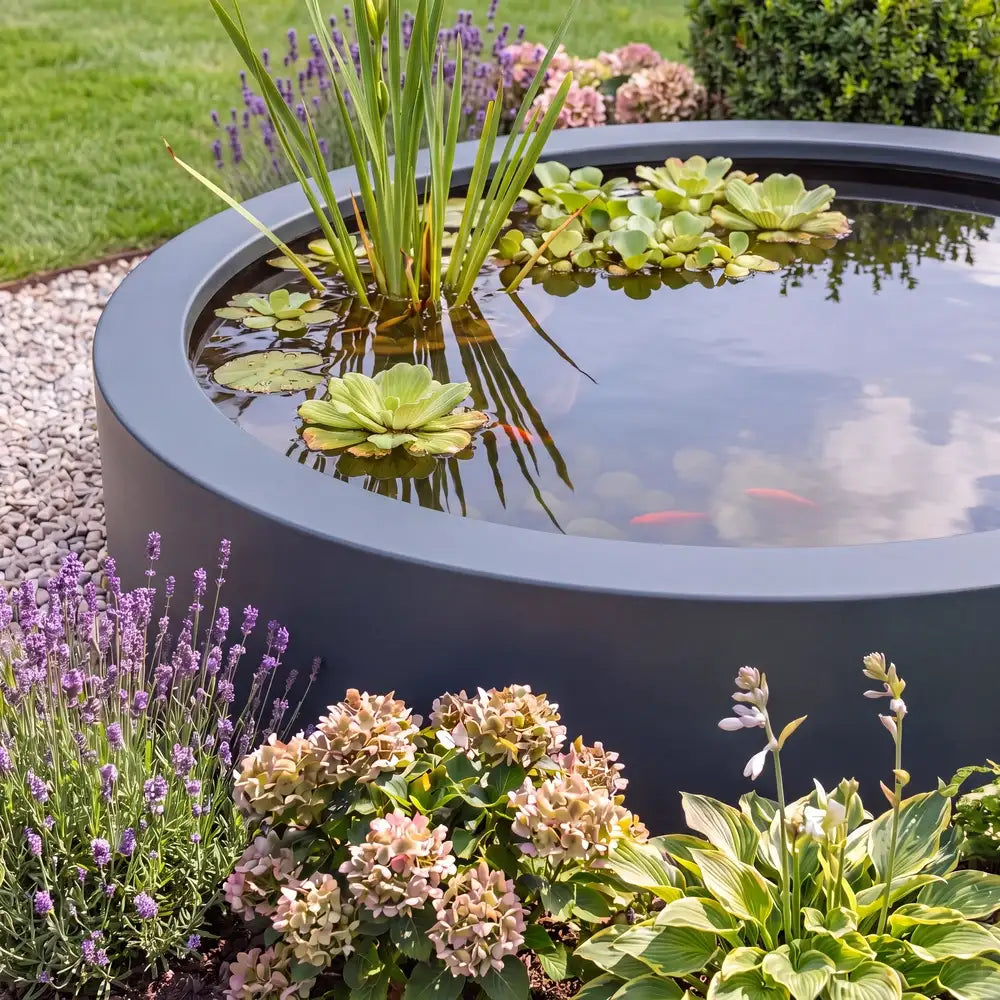 Rundes Wasserbecken aus Aluminium mit Pflanzen und Fischen in einem Blumenbeet im Garten.