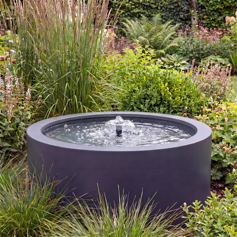 Rundes Alu-Teichbecken in einem Garten als Gartenbrunnen mit flacher Wasserfontäne.