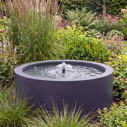 Rundes Alu-Teichbecken in einem Garten als Gartenbrunnen mit flacher Wasserfontäne.