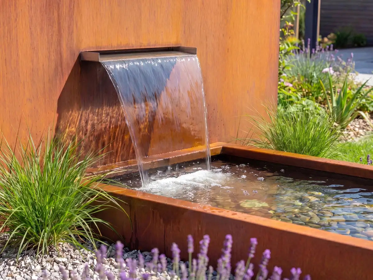 Cortenstahl-Wasserfall für einen Gartenteich in einem modernen Architektengarten mit Kiesboden und Pflanzen