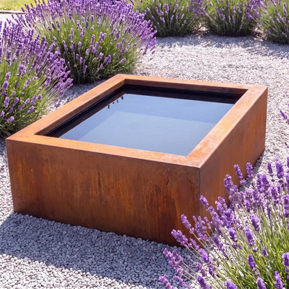 Cortenstahl-Hochteich in quadratischer Form mit spiegelnder Wasseroberfläche in einem minimalen Garten.