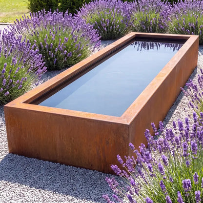 Rechteckiger Cortenstahl-Teich mit spiegelglatter Wasseroberfläche auf einer Fläche aus Kies und Lavendel-Pflanzen in einem modernen Garten.