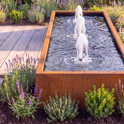 Rechteckiges Wasserbecken aus Cortenstahl mit Schaumsprudler und Wasserfontänen als Metall-Gartenbrunnen in einem modernen Garten.