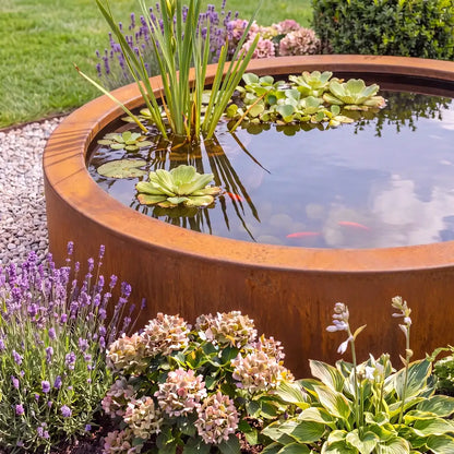 Rundes Wasserbecken aus Cortenstahl mit Pflanzen und Fischen in einem Blumenbeet im Garten.