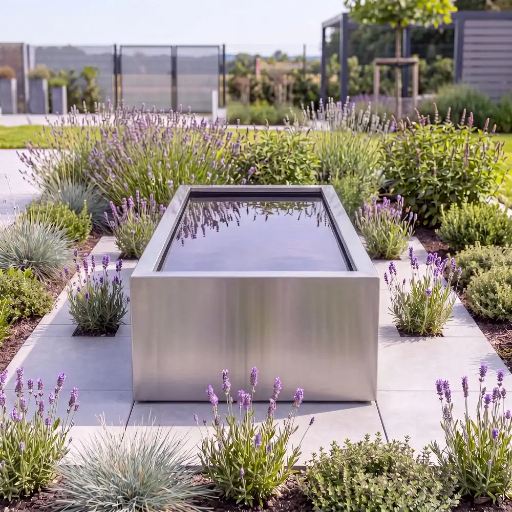 Rechteckiger Hochteich aus Edelstahl mit spiegelndem Wasser auf einer Pflasterfläche in einem modernen Design-Garten.