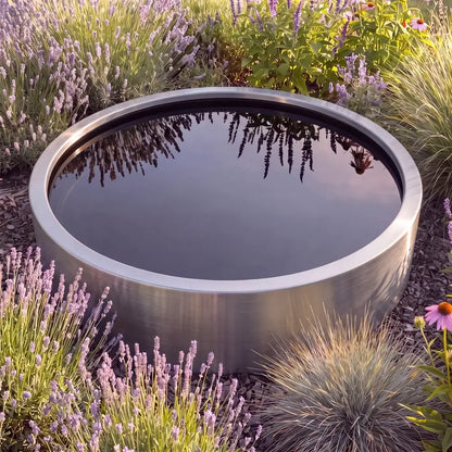 Runder Teich aus Edelstahl mit spiegelglatter Wasseroberfläche zwischen mediterranen Pflanzen in einem modernen Garten.