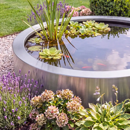 Rundes Wasserbecken aus Edelstahl mit Pflanzen und Fischen in einem Blumenbeet im Garten.