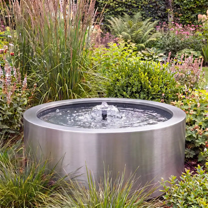 Rundes Metall-Teichbecken in einem Garten als Gartenbrunnen mit flacher Wasserfontäne.