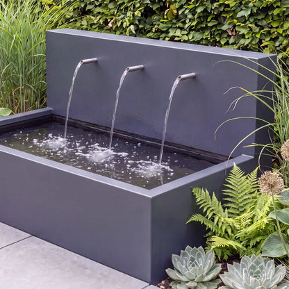 Kombination aus Wasserbecken mit einem Wasserfall aus Aluminium und Einlaufrohren vor einer Hecke im Außenbereich.