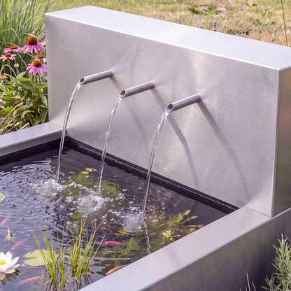 Großes Wasserfall-Element aus Edelstahl mit drei Wasserausläufen auf einem Metall-Wasserbecken in einem Garten.