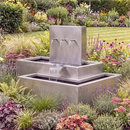 Wasserkaskade aus Edelstahl mit Einlaufrohren als Wasserspiel in einem bunten Blumenbeet.