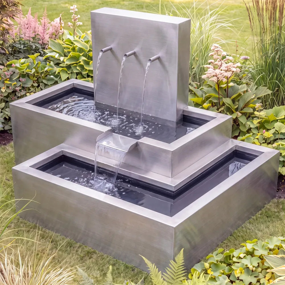 Metall-Wasserkaskade aus wetterfestem Edelstahl und Rohreinläufen auf einer grünen Rasenfläche im Garten.