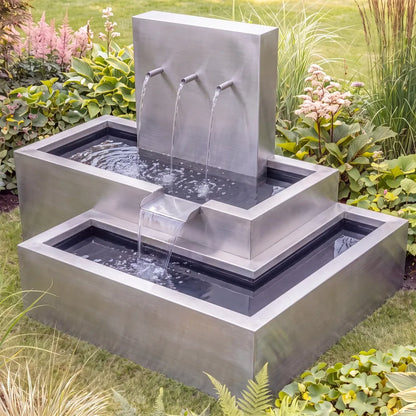 Metall-Wasserkaskade aus wetterfestem Edelstahl und Rohreinläufen auf einer grünen Rasenfläche im Garten.